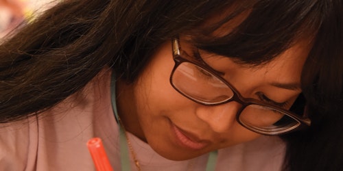 （被裁切的近距离照片）一名亚洲女孩戴着眼镜向下看，手里握着一支笔
