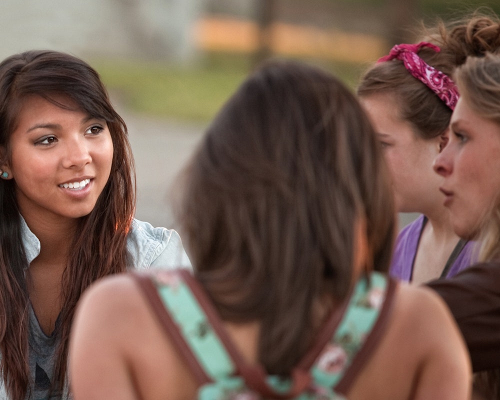 Foto de perto de um círculo de meninas conversando e olhando umas para as outras