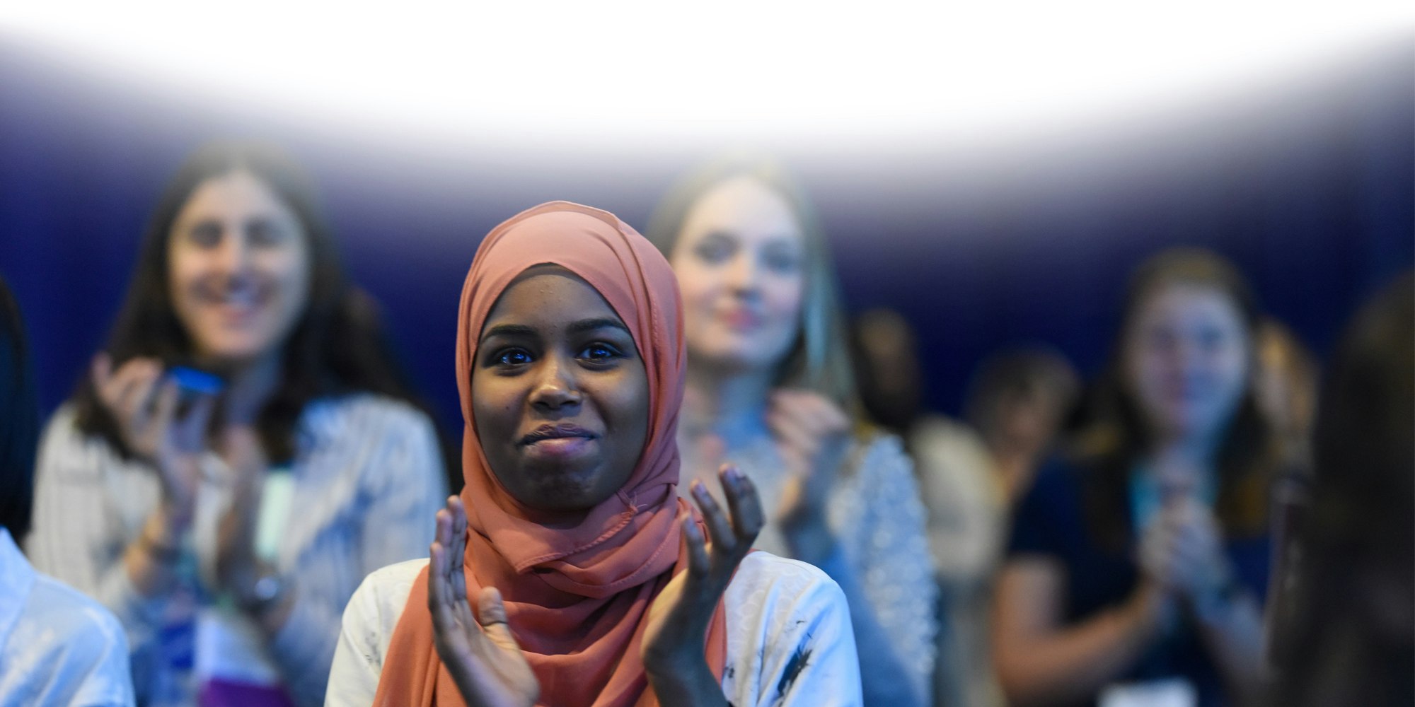 uma menina sorrindo com o seu Hijab rosa e batendo palmas