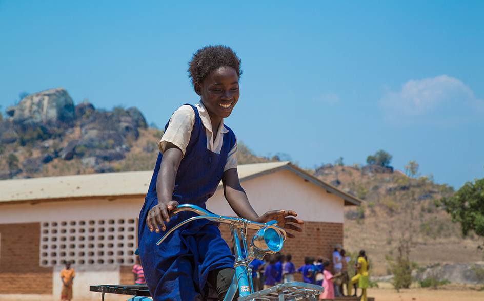 a girl with blue dress on the bicycle with a big smile on