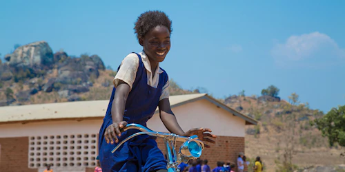 a girl with blue dress on the bicycle with a big smile on