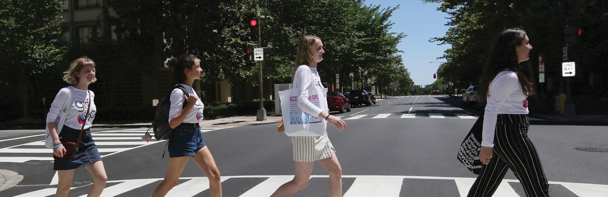 Meninas atravessando a rua em fila, olhando para frente e usando a camiseta de consultora adolescente