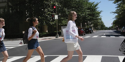 5 filles traversant la rue l’une après l’autre en regardant vers l’avant et portant leur maillot de Jeune conseillère