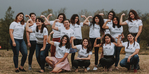 Um grupo de líderes Girl Up posam para a foto com os braços flexionados